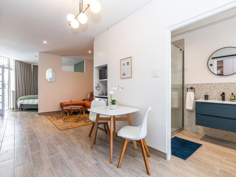 Modern open-plan apartment featuring wood-look tile flooring, recessed lighting, and a contemporary bathroom with a vanity and shower enclosure.