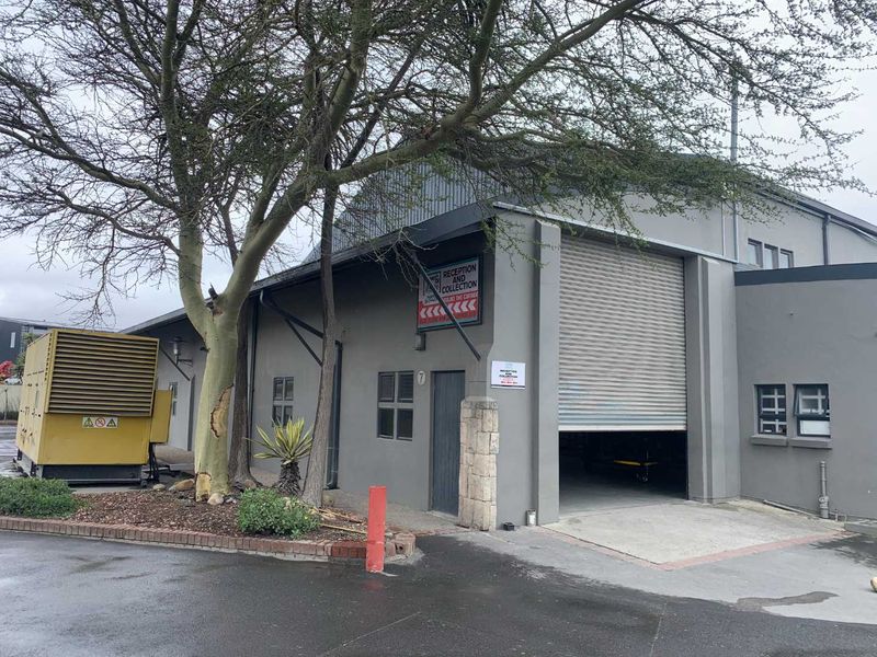 Industrial warehouse exterior featuring a large roller shutter door, metal roofing, and an external backup generator unit.