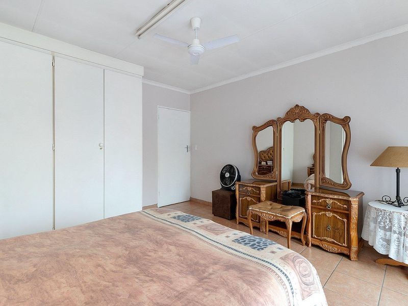 A bedroom featuring tiled flooring, built-in cupboards, and a ceiling fan.