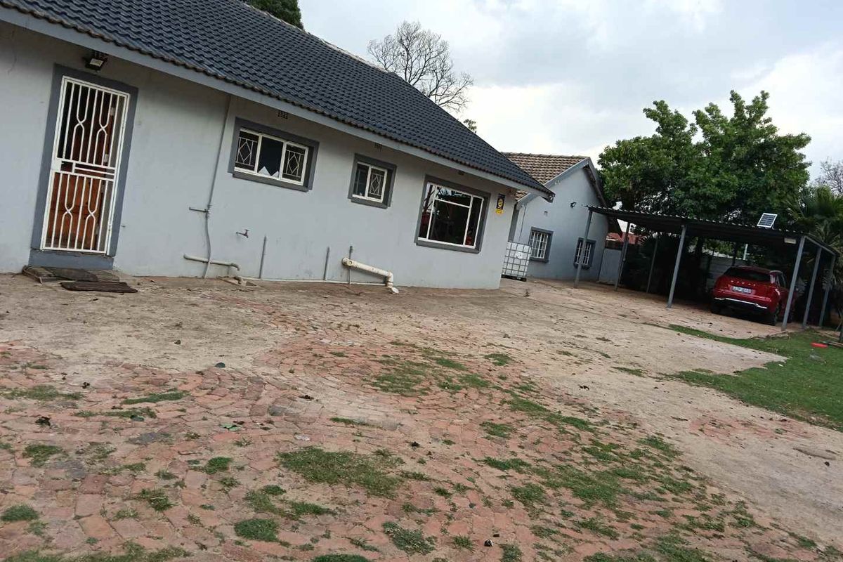 Rear exterior view of the property featuring a tiled roof, security gates, and a covered carport area with a paved driveway.