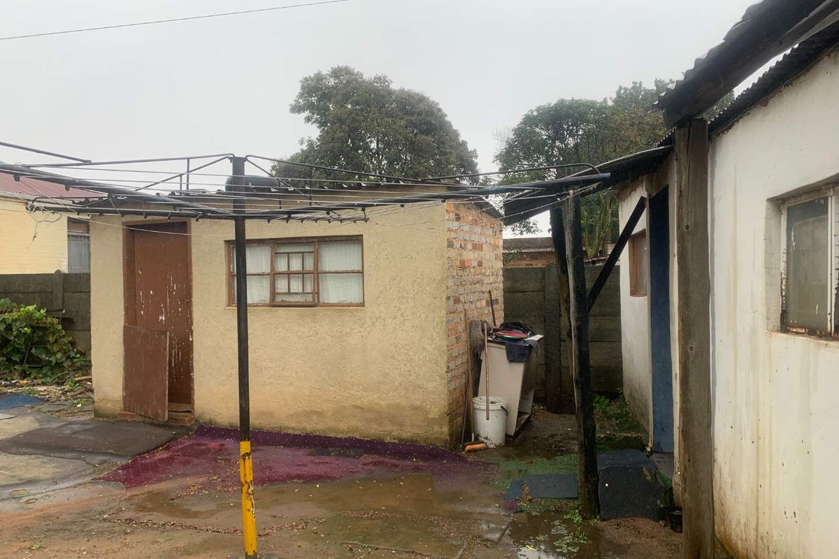 Rear exterior view of the property showing a small outbuilding, weathered walls, and a basic outdoor area with a rotary clothesline.
