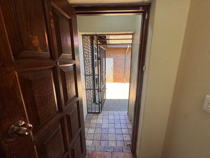 An entryway featuring a timber panel door leading to an exterior paved courtyard area secured by a metal security gate.