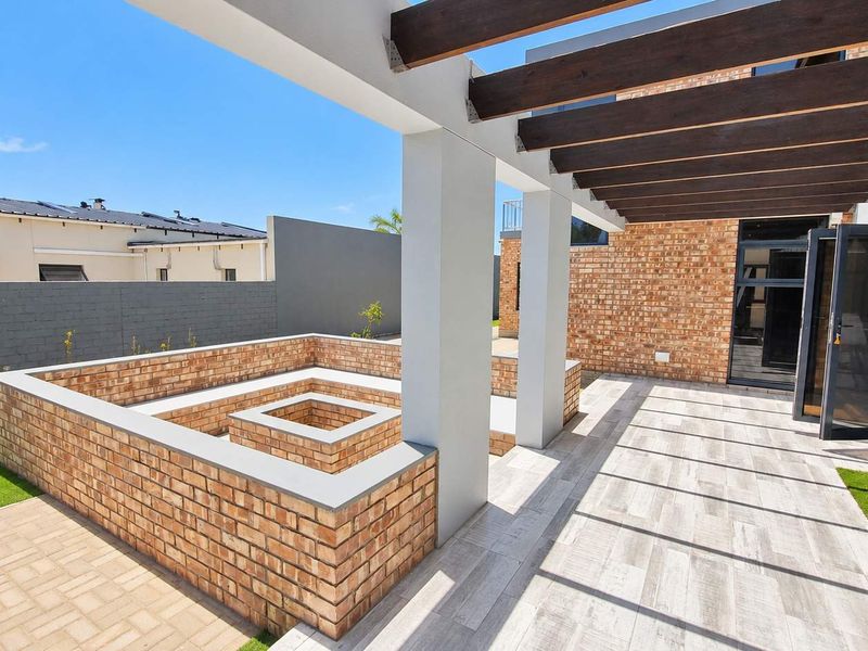 A modern outdoor patio featuring a timber pergola, a sunken brick fire pit, and seamless access to the interior through large sliding glass doors.