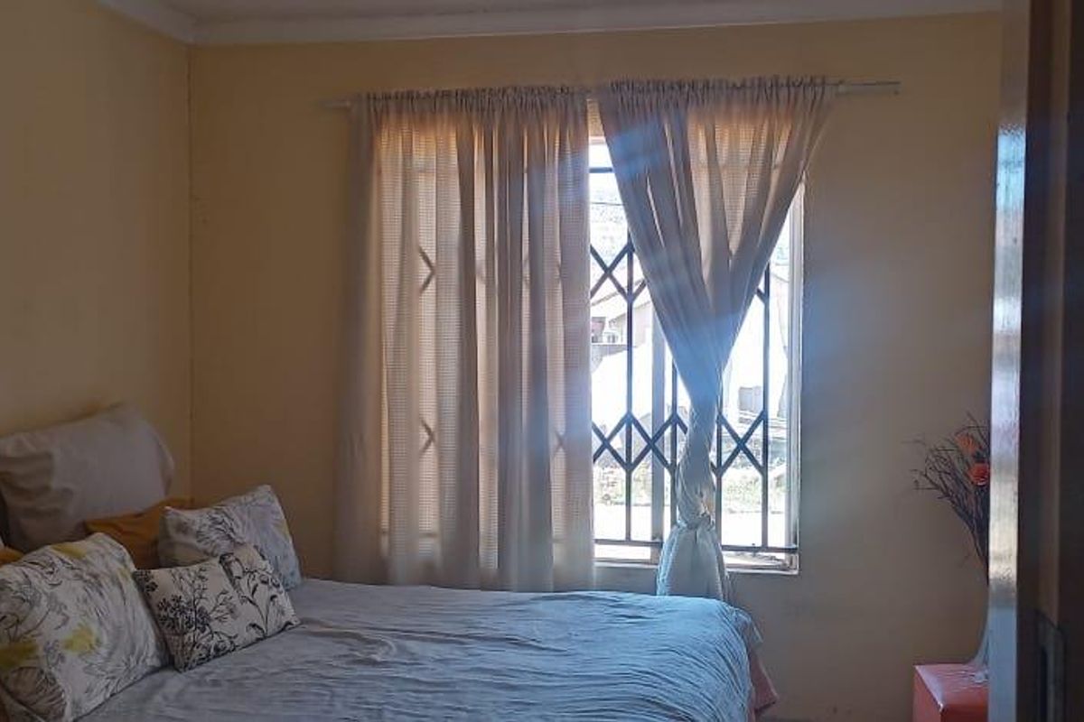 A bedroom featuring a window with security bars and curtains, providing natural light to the space.