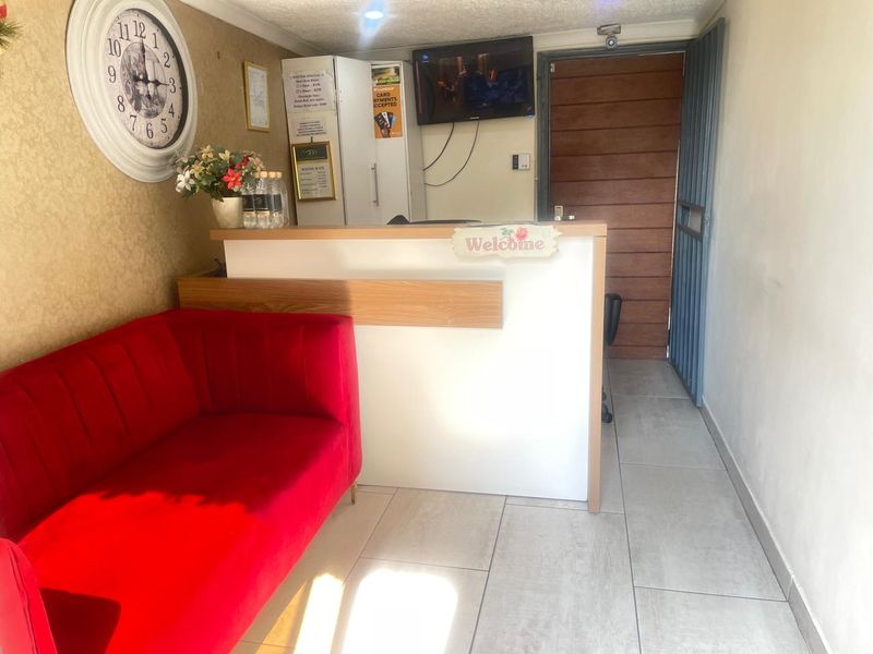 A functional guest house reception area featuring a built-in service counter, tiled flooring, and a secure entrance door.