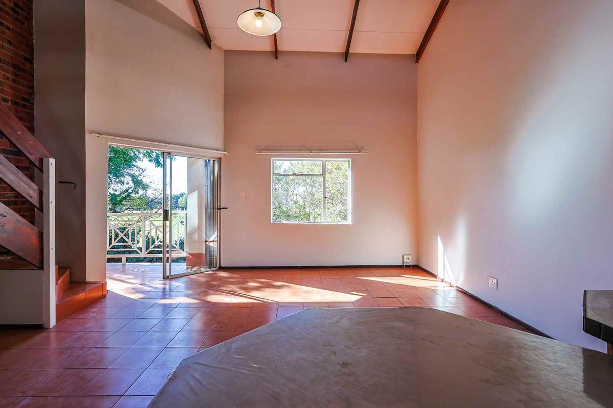 Spacious living area with high vaulted ceilings, tiled flooring, and direct access to a private balcony through sliding glass doors.