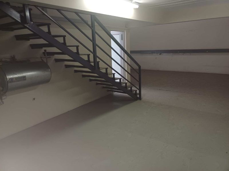 An open-plan industrial utility space featuring a metal staircase, wall-mounted water heater, and durable painted concrete flooring.