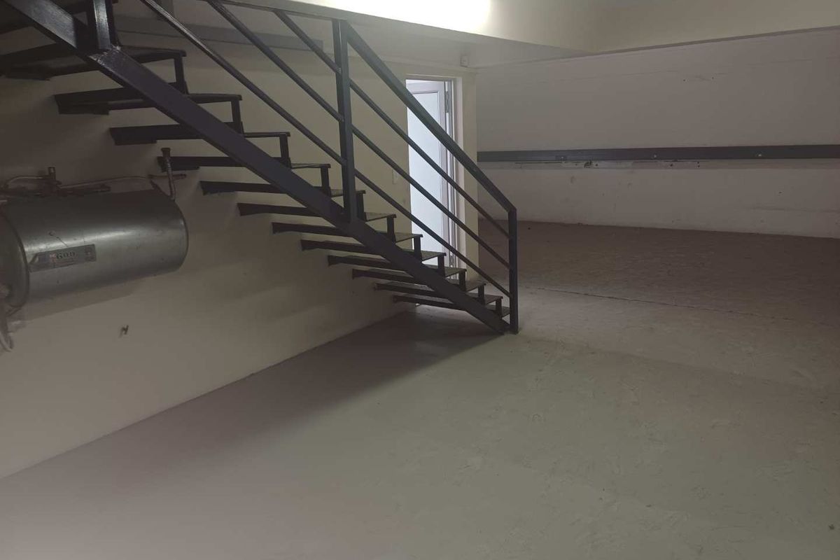 An open-plan industrial utility space featuring a metal staircase, wall-mounted water heater, and durable painted concrete flooring.