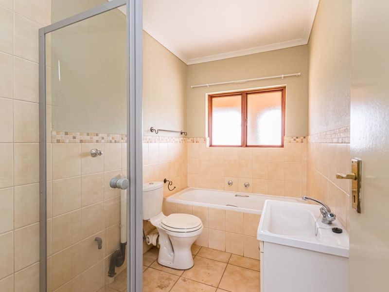 A functional bathroom featuring a shower enclosure, bathtub, toilet, and vanity basin with neutral wall and floor tiling.