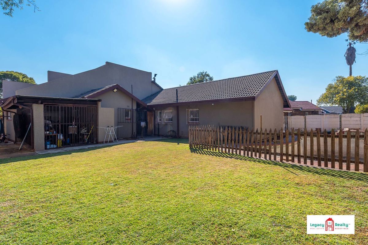 Rear view of the property featuring a spacious lawn, a fenced garden area, and a covered patio space with security gates.