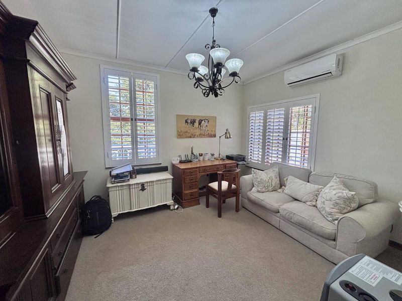 A well-maintained bedroom featuring neutral carpeting, plantation shutters for light control, a ceiling chandelier, and a wall-mounted split-system air conditioning unit.