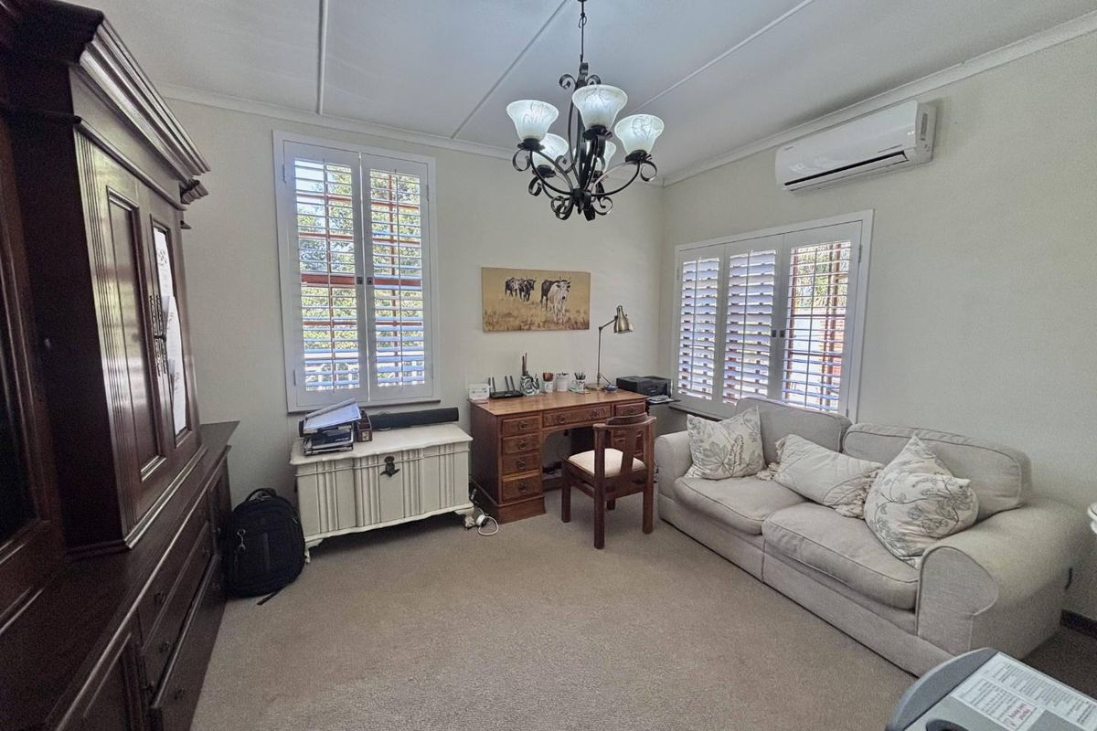 A well-maintained bedroom featuring neutral carpeting, plantation shutters for light control, a ceiling chandelier, and a wall-mounted split-system air conditioning unit.