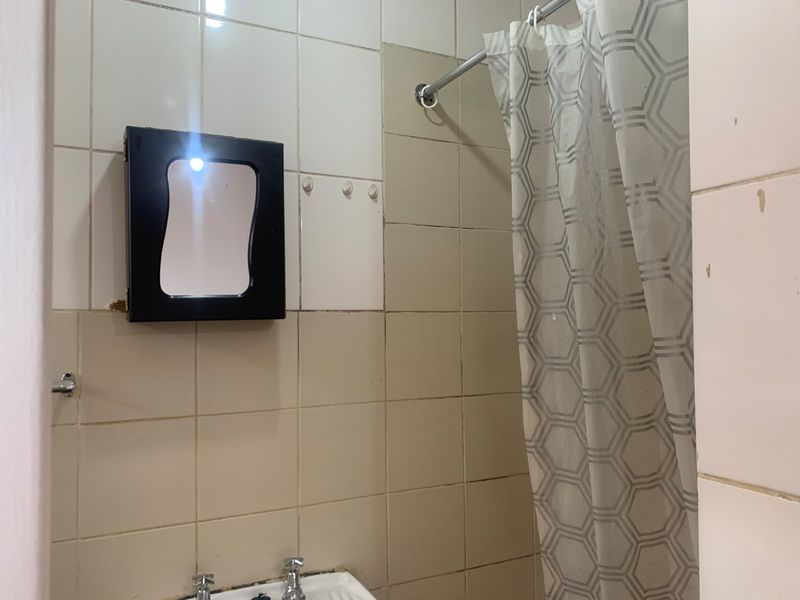 A functional bathroom area featuring tiled walls, a wall-mounted medicine cabinet, and a shower curtain setup, requiring cosmetic updates to improve its overall condition.