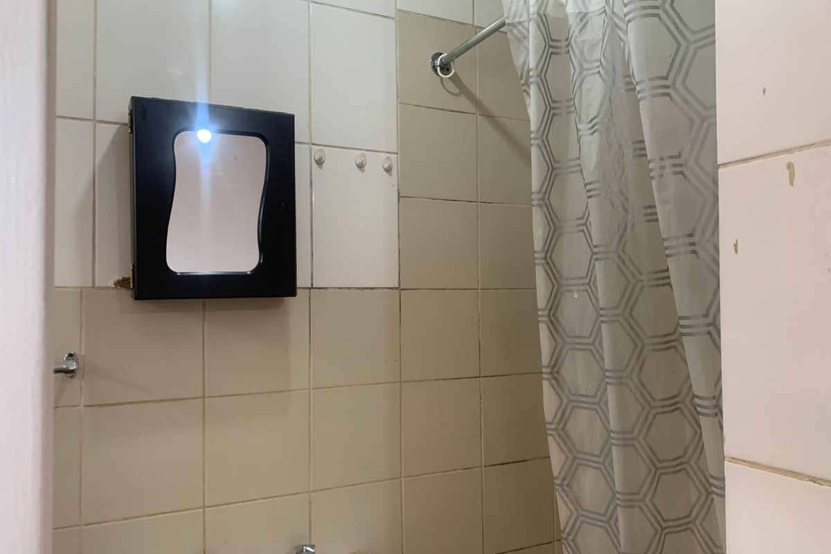 A functional bathroom area featuring tiled walls, a wall-mounted medicine cabinet, and a shower curtain setup, requiring cosmetic updates to improve its overall condition.