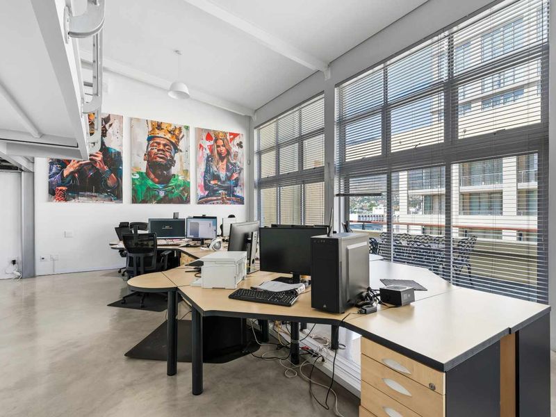 Modern office space featuring polished concrete floors, high ceilings with exposed beams, and large windows with venetian blinds providing ample natural light.