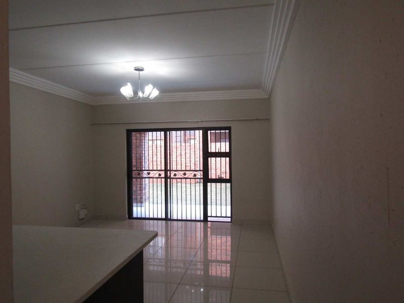 Spacious open-plan living area featuring tiled flooring, a ceiling cornice, and a sliding glass door with security gate leading to the exterior.