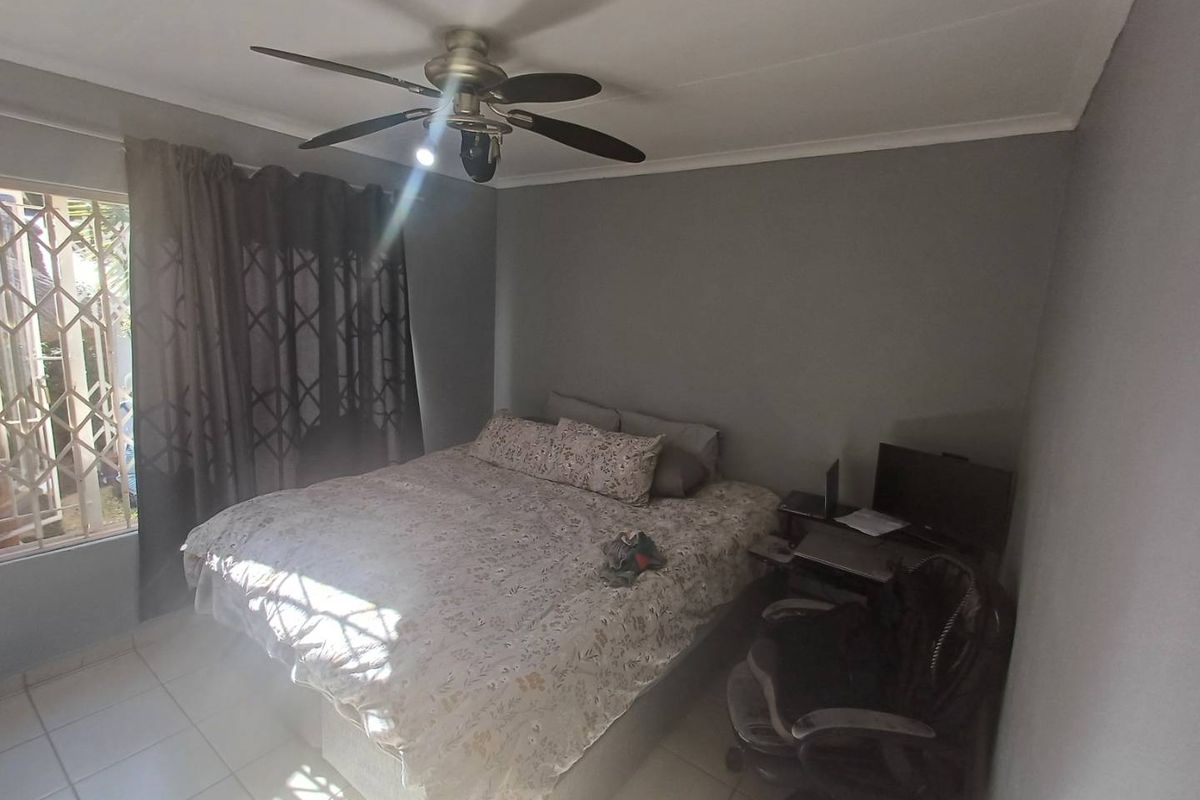 A bedroom featuring tiled flooring, a ceiling fan, and a security gate on the window, providing a functional and secure living space.