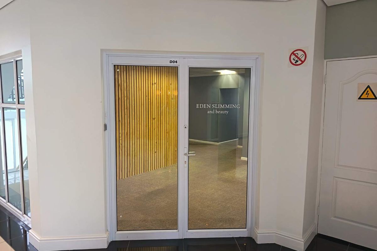 Entrance to a commercial unit featuring glass double doors with signage, set within a clean, modern hallway with tiled flooring.