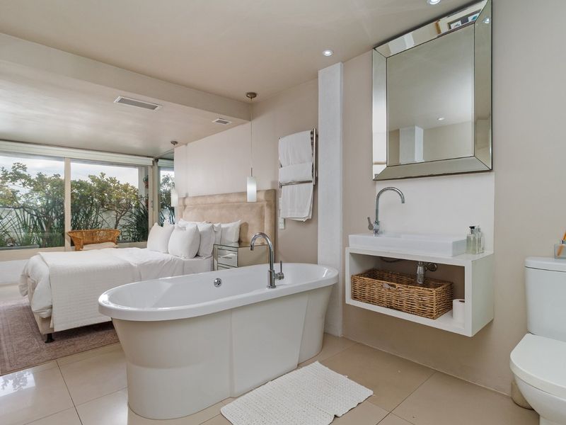 An open-plan bedroom suite featuring an integrated bathroom area with a freestanding bathtub, wall-mounted vanity, and sliding glass doors leading to the exterior.