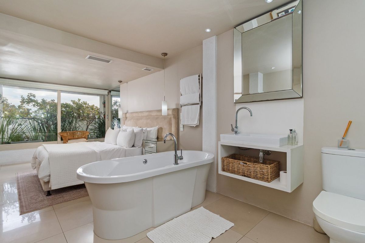 An open-plan bedroom suite featuring an integrated bathroom area with a freestanding bathtub, wall-mounted vanity, and sliding glass doors leading to the exterior.