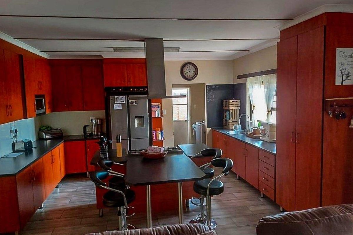 Spacious kitchen featuring wood-finish cabinetry, a central island with breakfast bar, stainless steel extractor fan, and tiled flooring.