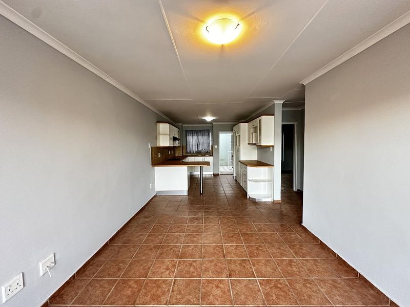 An open-plan living and kitchen area featuring tiled flooring, built-in cabinetry with laminate countertops, and neutral wall finishes.