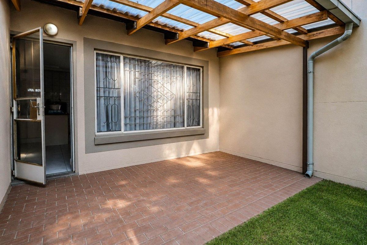 A covered patio area featuring brick paving, a timber pergola with translucent roofing, and direct access to the interior living space.