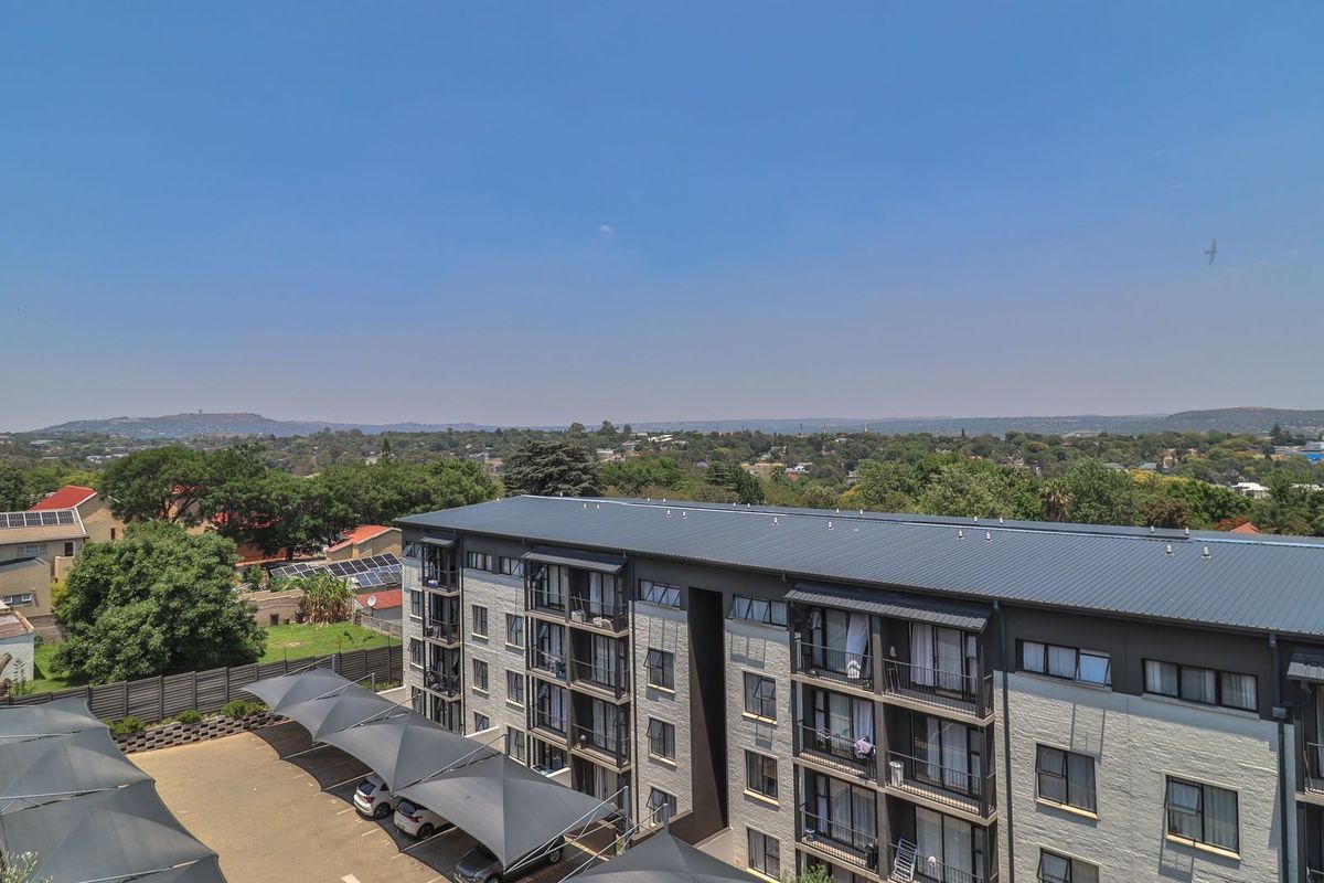 Aerial view of the apartment complex featuring a metal roof, private balconies, and covered parking bays within a landscaped residential setting.