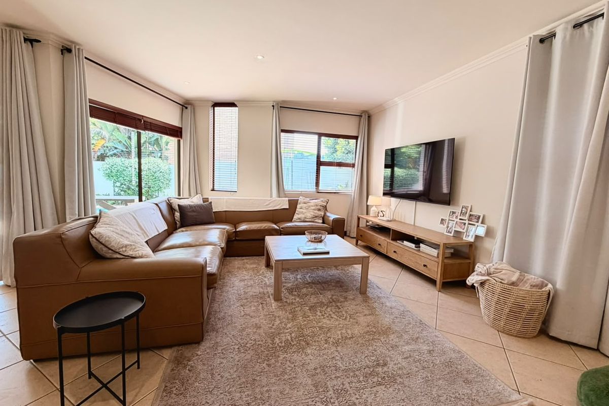 A bright and spacious living room featuring neutral tiled flooring, recessed lighting, and large windows that provide ample natural light and garden views.