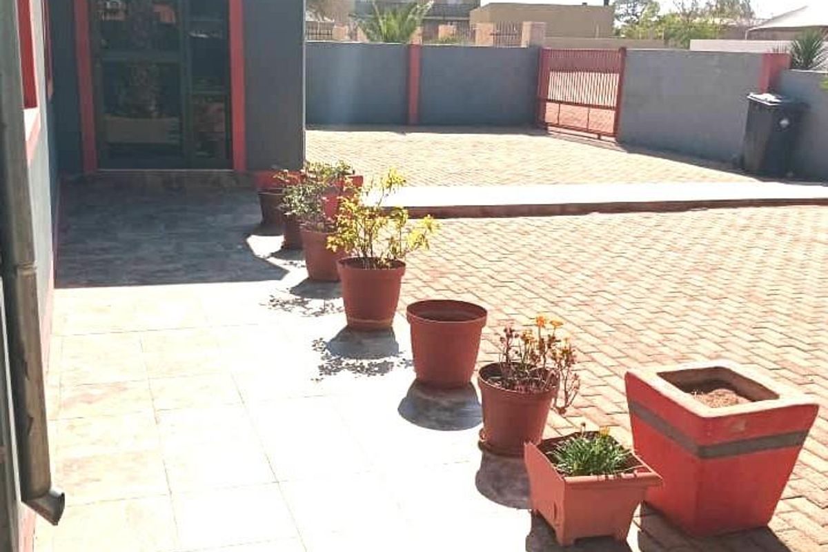 A paved rear courtyard area featuring a tiled patio section, perimeter boundary wall, and gated access.