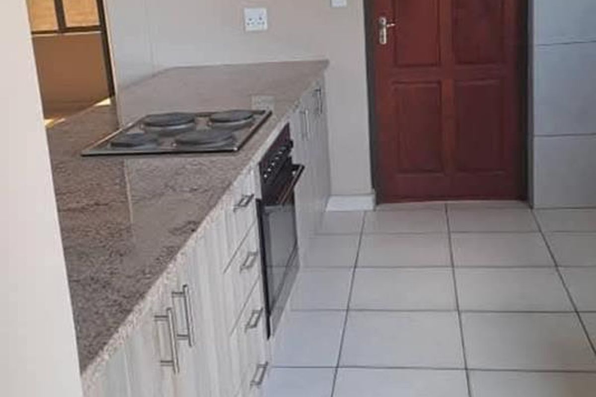 A functional kitchen featuring light wood-grain cabinetry, granite countertops, a built-in oven and hob, and tiled flooring.