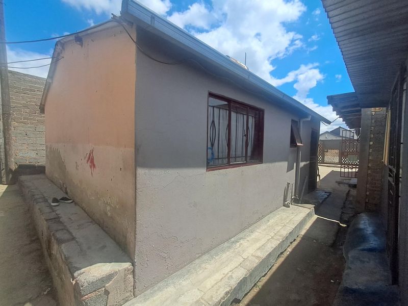 Rear exterior view of the property showing a single-story structure with metal window frames, security bars, and a concrete plinth foundation.
