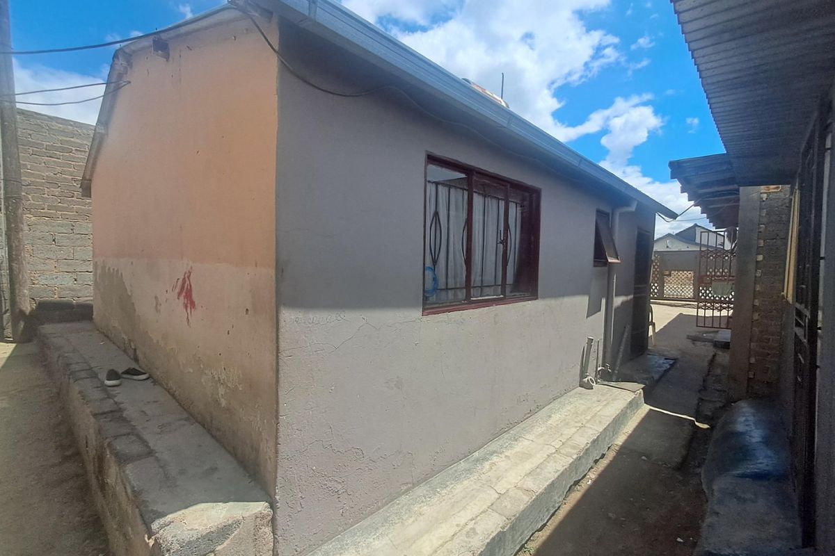 Rear exterior view of the property showing a single-story structure with metal window frames, security bars, and a concrete plinth foundation.