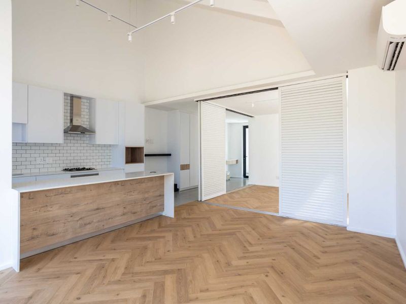 Modern open-plan living area featuring herringbone timber flooring, a sleek kitchen with subway tile backsplash, and a versatile sliding room divider.