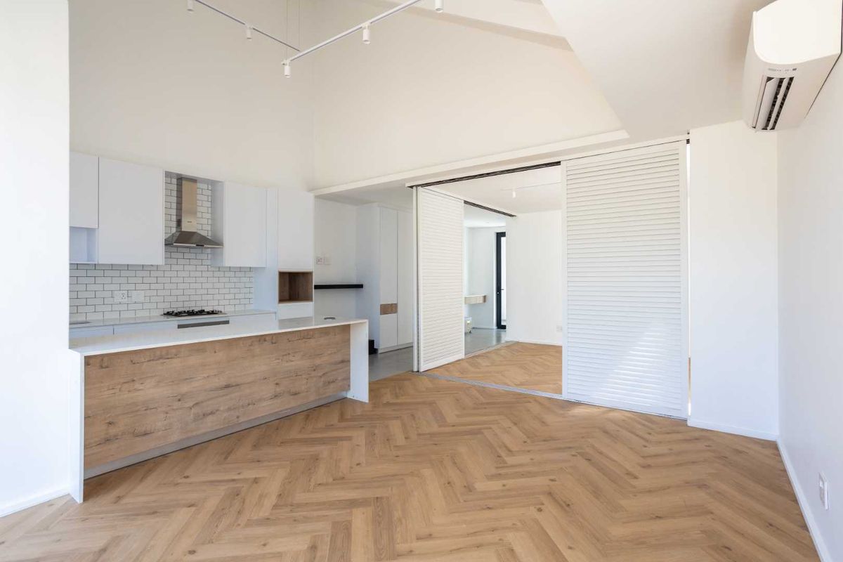 Modern open-plan living area featuring herringbone timber flooring, a sleek kitchen with subway tile backsplash, and a versatile sliding room divider.