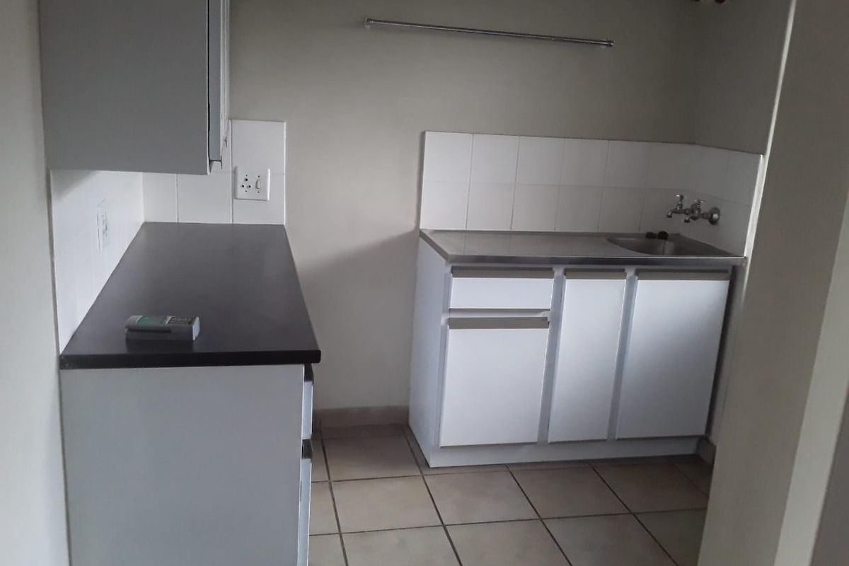 A functional kitchen area featuring white cabinetry, dark countertops, a stainless steel sink, and tiled flooring.