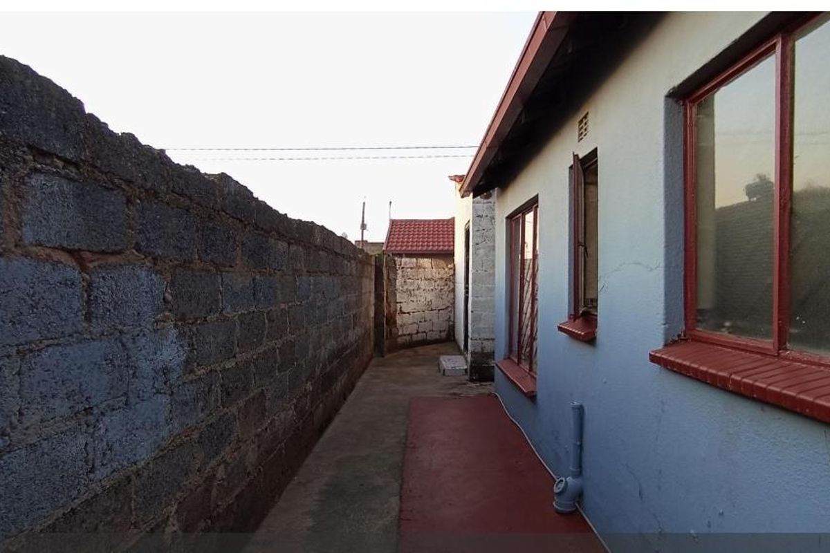 A narrow side passage of the house featuring a concrete pathway, boundary wall, and exterior wall with metal-framed windows.
