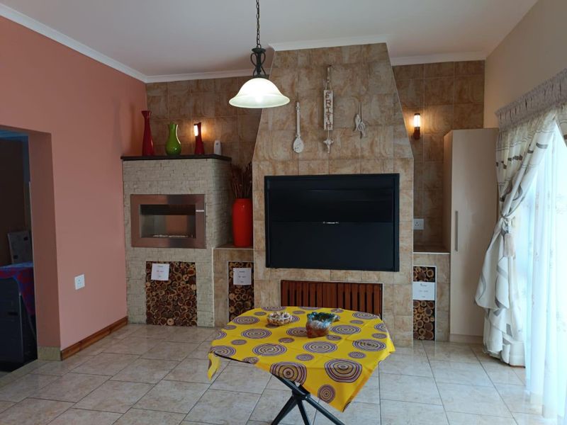 Living area featuring a prominent tiled fireplace and built-in braai, with neutral floor tiles and integrated storage cabinetry.