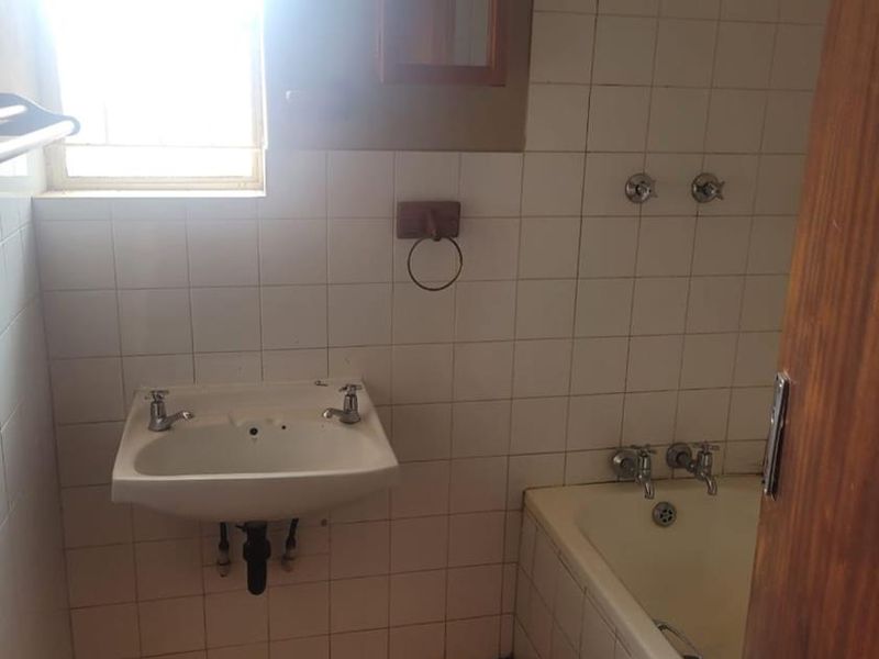 A dated bathroom featuring a wall-mounted basin, built-in bathtub, and tiled finishes, offering a blank canvas for a modern renovation.