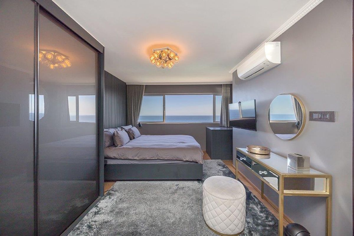 Modern bedroom featuring a built-in sliding wardrobe, slatted feature wall, split-system air conditioning, and expansive ocean views through large windows.