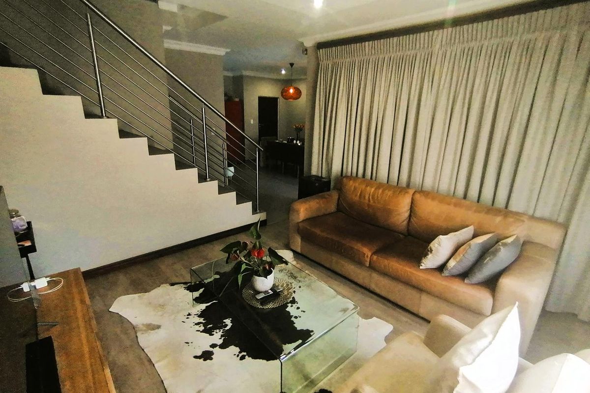 A well-maintained living room featuring a modern staircase with stainless steel balustrades, neutral flooring, and floor-to-ceiling curtains.