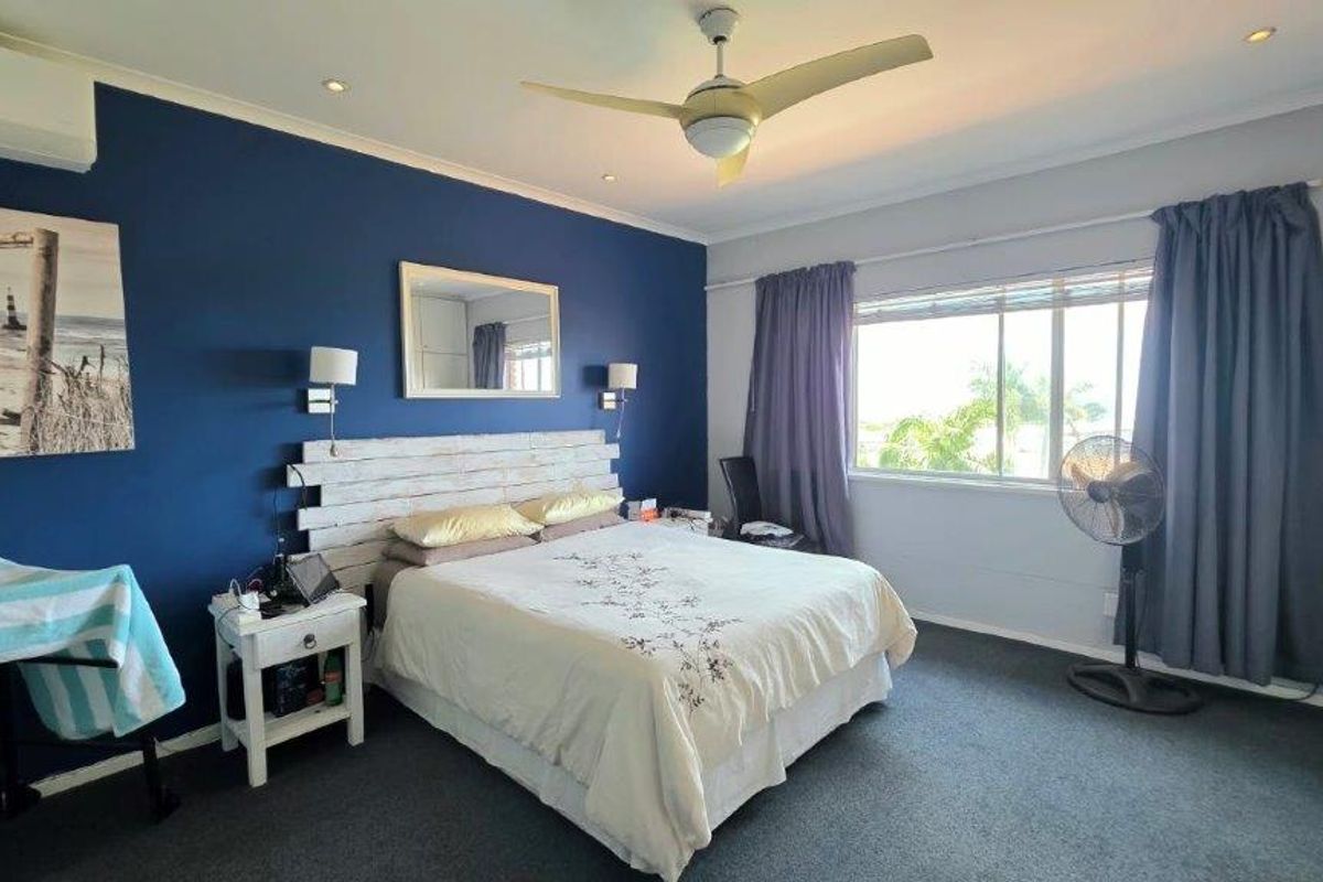 A spacious bedroom featuring a bold accent wall, built-in wardrobe, ceiling fan, and split-system air conditioning unit.