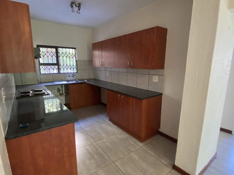 A functional kitchen featuring wooden cabinetry, granite countertops, a built-in hob, and tiled flooring, offering a clean and practical workspace.