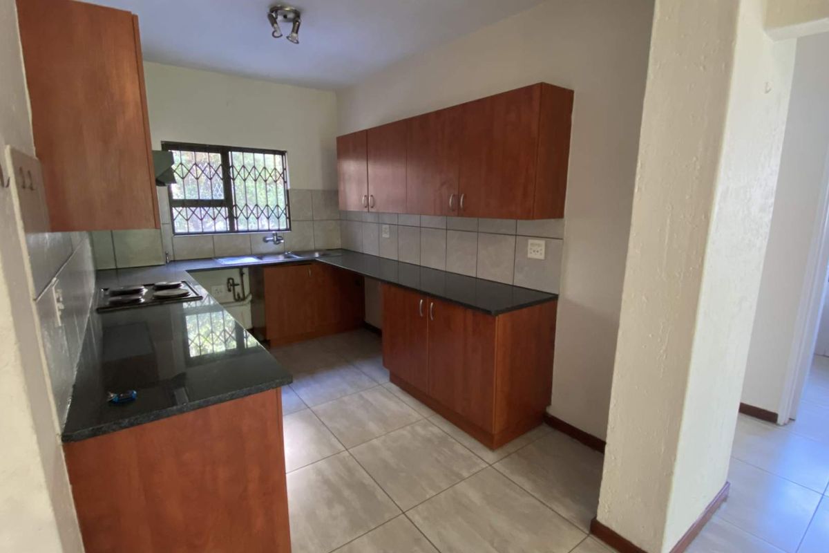 A functional kitchen featuring wooden cabinetry, granite countertops, a built-in hob, and tiled flooring, offering a clean and practical workspace.