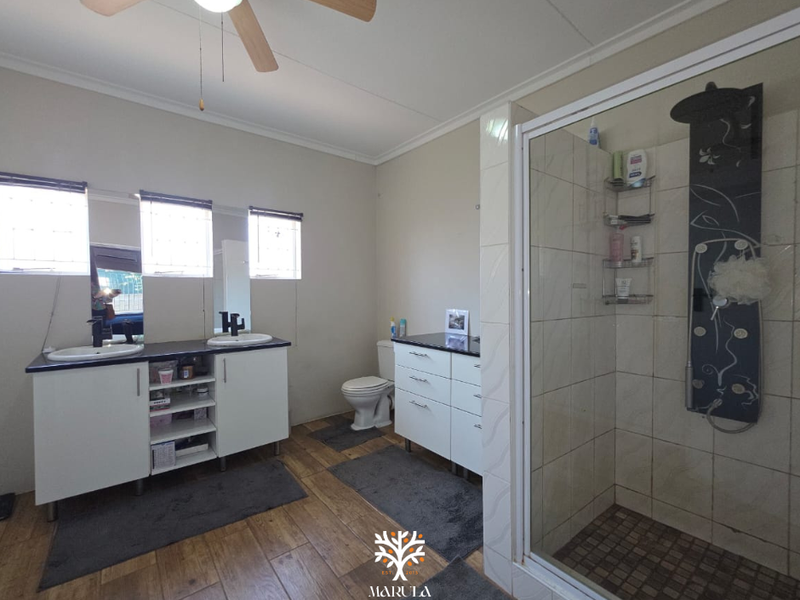 Spacious bathroom featuring a double vanity, a modern shower enclosure with a fitted shower panel, and tiled flooring.