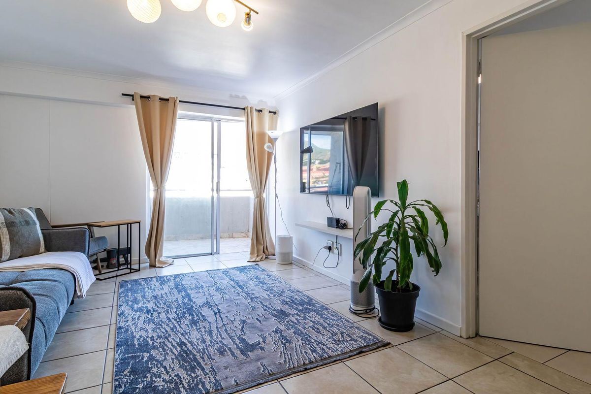 A bright living room featuring tiled flooring, a wall-mounted television, and sliding glass doors that open onto a balcony.