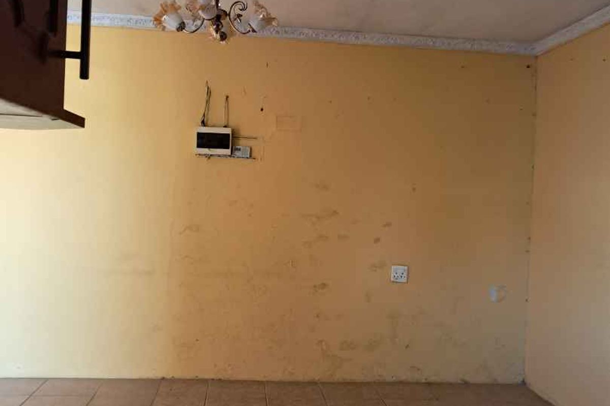 An empty living area featuring tiled flooring, a decorative chandelier, and wall surfaces requiring maintenance and repainting.