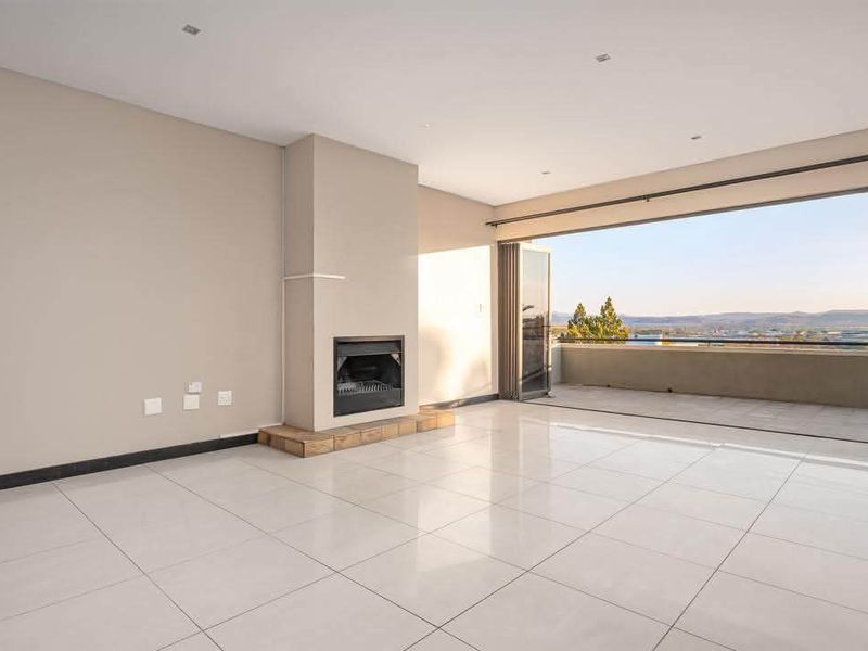 Spacious open-plan living area featuring large format floor tiles, a built-in fireplace, and seamless access to a balcony through stacking glass doors.