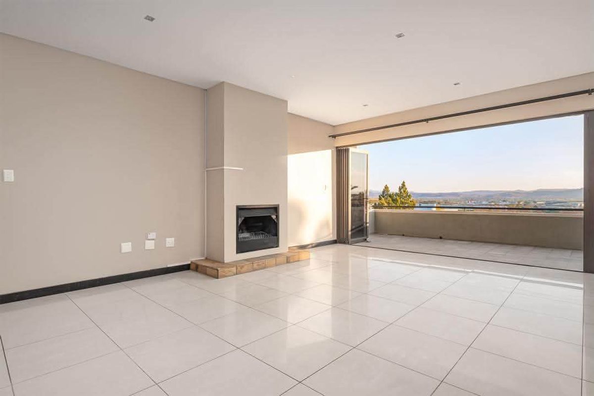 Spacious open-plan living area featuring large format floor tiles, a built-in fireplace, and seamless access to a balcony through stacking glass doors.