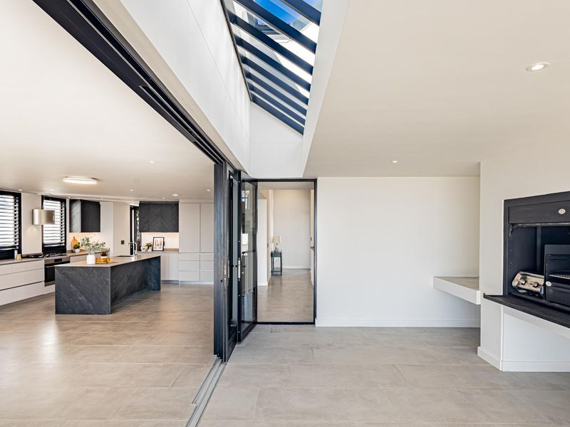 Spacious open-plan living area featuring a modern kitchen with island, skylight, and a built-in indoor braai, seamlessly connecting to the outdoor patio space.